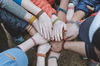 Group of students with hands stacked together, wearing colorful handwoven bracelets.